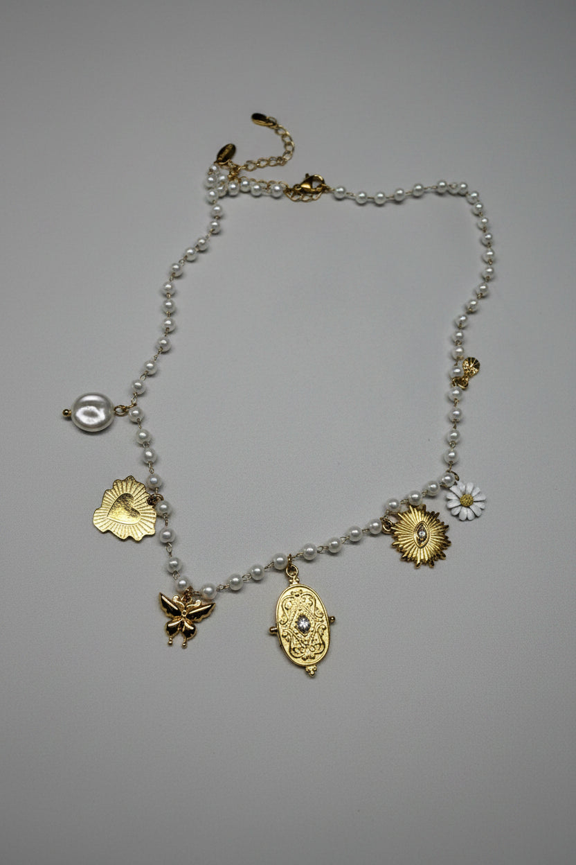 Collana a filo di perle bianche con 5 charm dorati: cuore sacro, farfalla, medaglione barocco, sole con cristallo e margherita smaltata