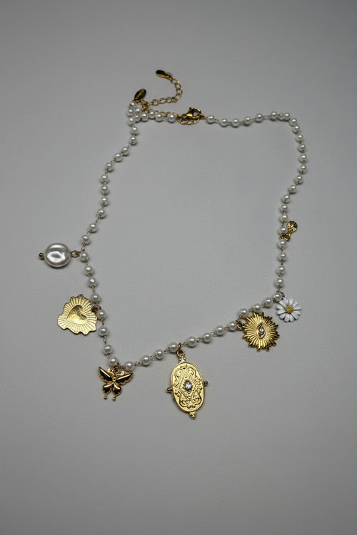 Collana a filo di perle bianche con 5 charm dorati: cuore sacro, farfalla, medaglione barocco, sole con cristallo e margherita smaltata